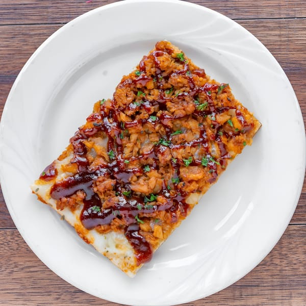 A rectangular slice of Garlic New York Pizza Bar's BBQ chicken pizza on a white plate.