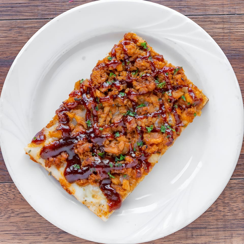 A rectangular slice of Garlic New York Pizza Bar's BBQ chicken pizza on a white plate.