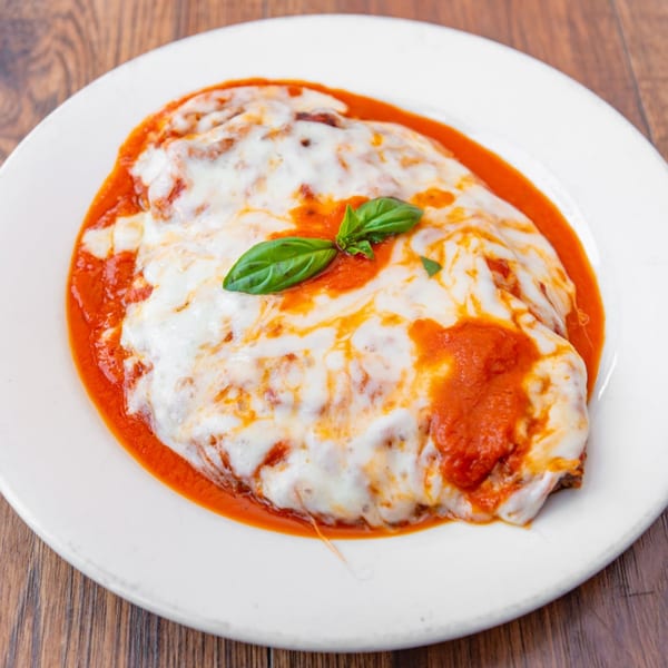 Eggplant Parmesan with melted mozzarella cheese, marinara sauce, and fresh basil on a white plate.